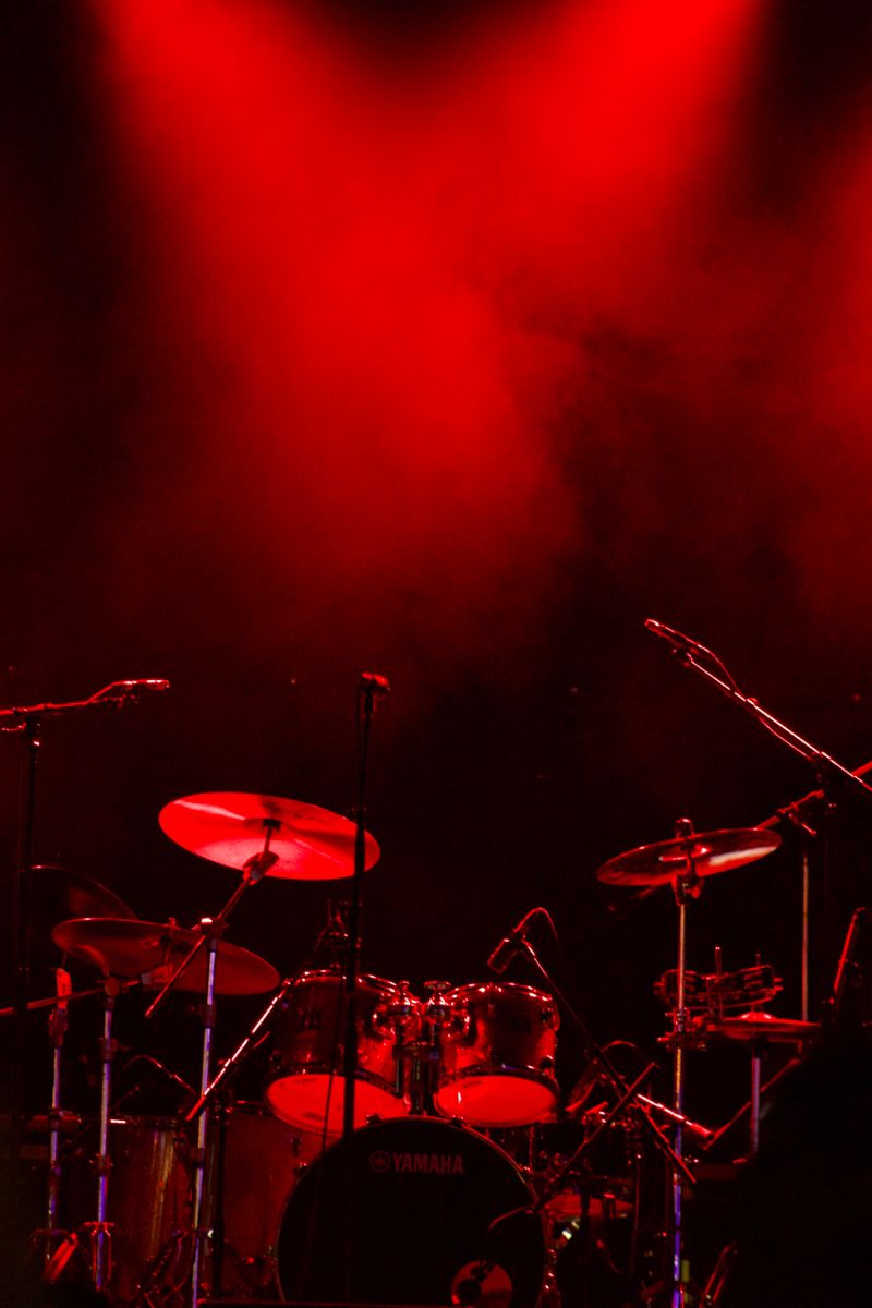 Drum kit set on stage under dramatic red spotlighting for Mindwork School Of Music website about page.